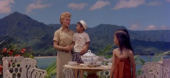 Movie still from “South Pacific” (1958), directed by Joshua Logan – A woman and two children standing at a table; Medium shot, High angle