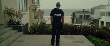 Movie still from “Southland Tales” (2006), directed by Richard Kelly – A police officer standing on a sidewalk looking out at the beach; Wide shot, Low angle