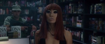 Movie still from “Southland Tales” (2006), directed by Richard Kelly – A woman with red hair smoking a cigarette in front of a book shelf; Close Up shot, Over the shoulder angle