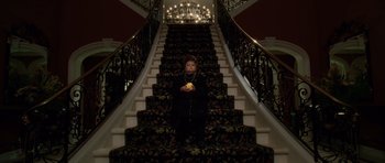 Movie still from “Southland Tales” (2006), directed by Richard Kelly – A woman sitting on the bottom step of a stair case holding an apple; Wide shot, High angle
