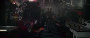 Two men in military fatigues walking through a room full of chairs