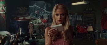 Movie still from “Southland Tales” (2006), directed by Richard Kelly – A woman in a pink dress holding a white card; Close Up shot, Over the shoulder angle