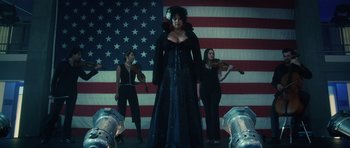 Movie still from “Southland Tales” (2006), directed by Richard Kelly – A woman in a black dress stands in front of two other women; Wide shot, Low angle