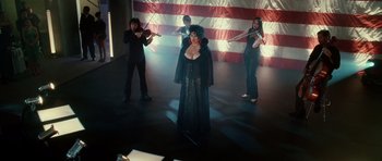 Movie still from “Southland Tales” (2006), directed by Richard Kelly – A group of people playing musical instruments in front of an american flag; Wide shot, High angle