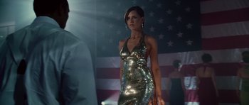 Movie still from “Southland Tales” (2006), directed by Richard Kelly – A woman in a silver sequined dress standing in front of an american flag; Medium shot, Low angle
