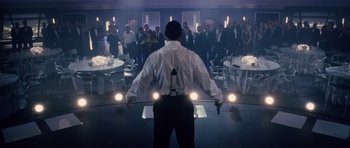 Movie still from “Southland Tales” (2006), directed by Richard Kelly – A man standing in front of a group of people in a room; Wide shot, Low angle