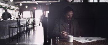 Movie still from “A Walk Among the Tombstones” (2014), directed by Scott Frank – A man sitting at a table with a cup of coffee; Medium shot, Low angle