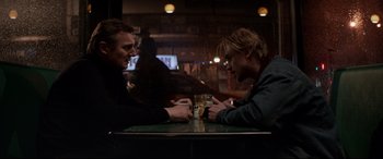 Movie still from “A Walk Among the Tombstones” (2014), directed by Scott Frank – Two men sitting at a table with a drink in front of them; Medium shot, Over the shoulder angle