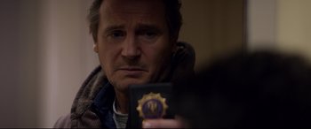 Movie still from “A Walk Among the Tombstones” (2014), directed by Scott Frank – A man looking at the camera while holding a passport; Close Up shot, Over the shoulder angle