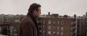 Movie still from “A Walk Among the Tombstones” (2014), directed by Scott Frank – A man standing on a balcony looking out at a building; Medium shot, Low angle