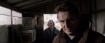 Movie still from “A Walk Among the Tombstones” (2014), directed by Scott Frank – A man standing next to another man in a room; Close Up shot, Over the shoulder angle