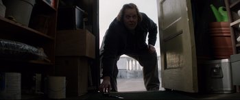 Movie still from “A Walk Among the Tombstones” (2014), directed by Scott Frank – A man standing in front of an open door; Medium shot, Low angle