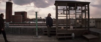 Movie still from “A Walk Among the Tombstones” (2014), directed by Scott Frank – A man standing in front of a bird cage; Wide shot, Low angle