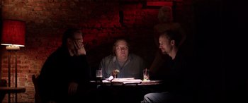Movie still from “A Walk Among the Tombstones” (2014), directed by Scott Frank – A group of men sitting at a table in a dark room; Medium shot, Over the shoulder angle