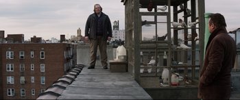 Movie still from “A Walk Among the Tombstones” (2014), directed by Scott Frank – A man standing on a platform in front of a bird cage; Wide shot, Low angle