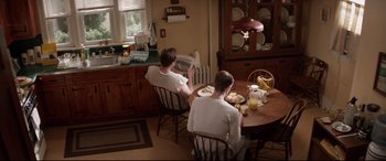 Movie still from “A Walk Among the Tombstones” (2014), directed by Scott Frank – Two young men sitting at a table in a kitchen; Wide shot, High angle