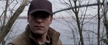 Movie still from “A Walk Among the Tombstones” (2014), directed by Scott Frank – A person wearing a hat near a body of water; Close Up shot, Over the shoulder angle