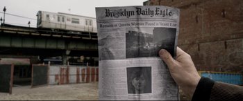 Movie still from “A Walk Among the Tombstones” (2014), directed by Scott Frank – A person holding a newspaper in front of a building; Extreme Close Up shot, High angle