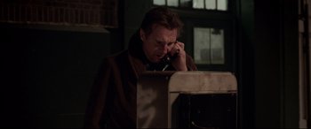 Movie still from “A Walk Among the Tombstones” (2014), directed by Scott Frank – A man talking on a phone while sitting in front of a computer; Medium shot, Low angle