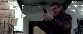 Movie still from “A Walk Among the Tombstones” (2014), directed by Scott Frank – A man holding a gun in a room; Medium shot, Low angle