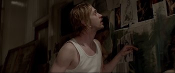 Movie still from “A Walk Among the Tombstones” (2014), directed by Scott Frank – A man in a white tank top looking up at a picture; Close Up shot, Over the shoulder angle