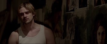 Movie still from “A Walk Among the Tombstones” (2014), directed by Scott Frank – A woman in a white tank top standing in front of a wall; Close Up shot, Over the shoulder angle