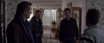 Movie still from “A Walk Among the Tombstones” (2014), directed by Scott Frank – A group of people standing in a room; Medium shot, Over the shoulder angle
