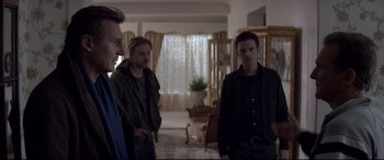 Movie still from “A Walk Among the Tombstones” (2014), directed by Scott Frank – A group of people standing in a room; Medium shot, Over the shoulder angle