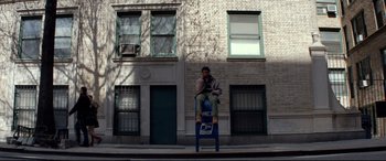 Movie still from “A Walk Among the Tombstones” (2014), directed by Scott Frank – A man sitting on top of a post on a sidewalk; Wide shot, Low angle