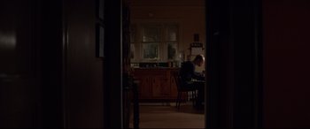 Movie still from “A Walk Among the Tombstones” (2014), directed by Scott Frank – A man sitting at a table in a room; Wide shot, Low angle