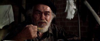 Movie still from “Soylent Green” (1973), directed by Richard Fleischer – An old man with a beard and a hat is holding a toothbrush in his mouth; Close Up shot, Low angle