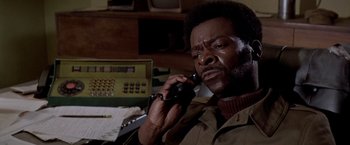 Movie still from “Soylent Green” (1973), directed by Richard Fleischer – A man talking on a phone while sitting at a desk; Close Up shot, Low angle