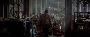 Movie still from “Soylent Green” (1973), directed by Richard Fleischer – A group of people sitting in a room with a cross on the wall; Wide shot, High angle