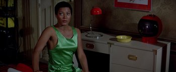 Movie still from “Soylent Green” (1973), directed by Richard Fleischer – A woman in a green dress sitting in front of a desk; Medium shot, High angle