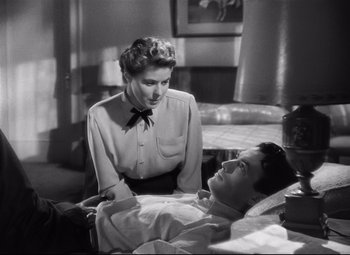 Movie still from “Spellbound” (1945), directed by Alfred Hitchcock – A woman standing next to a man laying on a bed; Medium shot, High angle