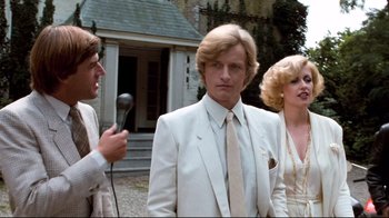 Movie still from “Spetters” (1980), directed by Paul Verhoeven – A man in a white suit is being interviewed by two other people; Medium shot, Low angle