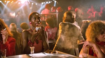 Movie still from “Spetters” (1980), directed by Paul Verhoeven – A woman sitting at a table eating a doughnut; Medium shot, Over the shoulder angle