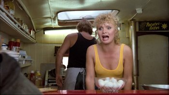 Movie still from “Spetters” (1980), directed by Paul Verhoeven – A woman in a yellow shirt is holding a bowl of eggs; Medium shot, Low angle