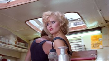 Movie still from “Spetters” (1980), directed by Paul Verhoeven – A woman with blonde curly hair is standing next to another woman; Medium shot, Low angle