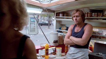 Movie still from “Spetters” (1980), directed by Paul Verhoeven – A man and a woman standing in front of a table; Medium shot, Low angle