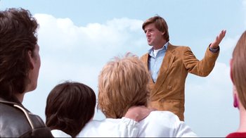 Movie still from “Spetters” (1980), directed by Paul Verhoeven – A man standing in front of a group of people; Medium shot, Low angle