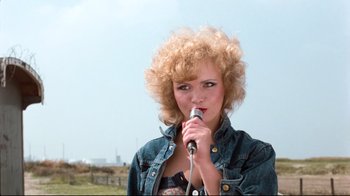 Movie still from “Spetters” (1980), directed by Paul Verhoeven – A woman holding a microphone up to her mouth; Close Up shot, Low angle