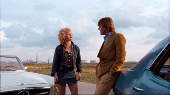 Movie still from “Spetters” (1980), directed by Paul Verhoeven – A man and a woman standing next to each other on the side of a road; Wide shot, Low angle