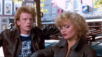 Movie still from “Spetters” (1980), directed by Paul Verhoeven – A man and a woman sitting next to each other on the street; Medium shot, Over the shoulder angle