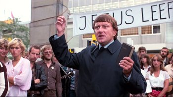Movie still from “Spetters” (1980), directed by Paul Verhoeven – A man holding a book in front of a group of people; Medium shot, Low angle