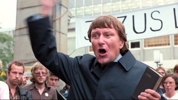 Movie still from “Spetters” (1980), directed by Paul Verhoeven – A man in a black shirt is holding his hand up in the air; Close Up shot, Low angle