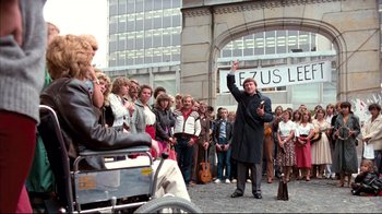Movie still from “Spetters” (1980), directed by Paul Verhoeven – A crowd of people standing in front of a building; Wide shot, Over the shoulder angle