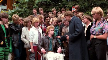 Movie still from “Spetters” (1980), directed by Paul Verhoeven – A group of people gathered around a man in a wheelchair; Wide shot, Over the shoulder angle