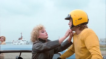 Movie still from “Spetters” (1980), directed by Paul Verhoeven – A woman adjusts the helmet of a young man; Medium shot, Over the shoulder angle