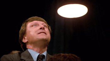 Movie still from “Spetters” (1980), directed by Paul Verhoeven – A man in a suit and tie looking up at a light; Close Up shot, Low angle